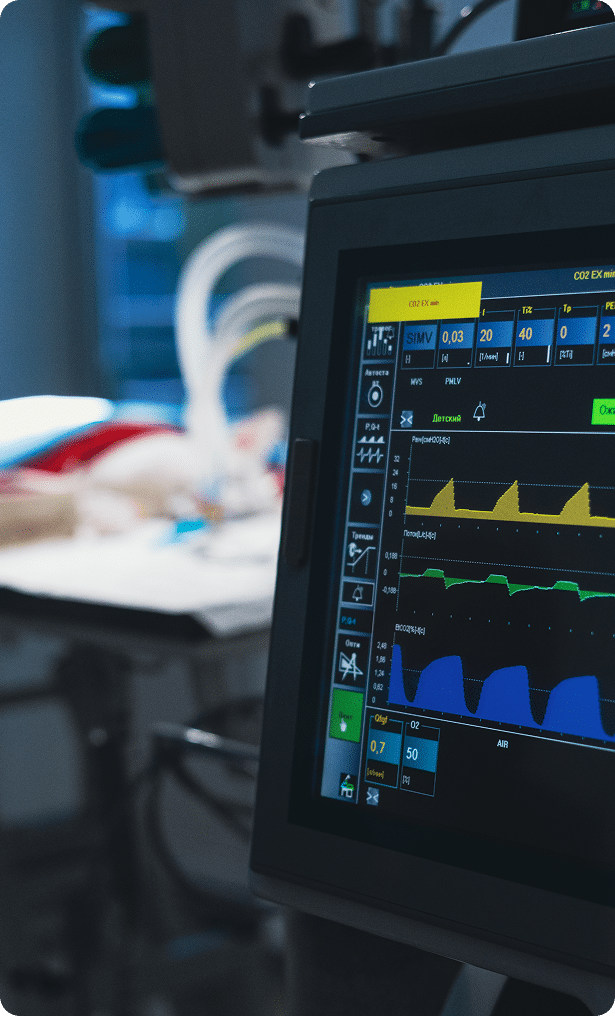 A close-up of a medical monitor displaying patient vital signs, with blurred hospital equipment in the background.